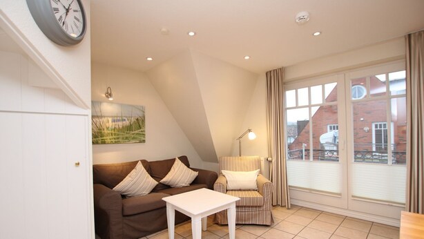 Een gezellige woonkamer met een bruine bank, een gestreept fauteuil, een witte salontafel en een groot raam met gordijnen.