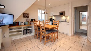 Een moderne keuken met een eethoek, met een houten tafel en stoelen, een televisie en een boekenkast.