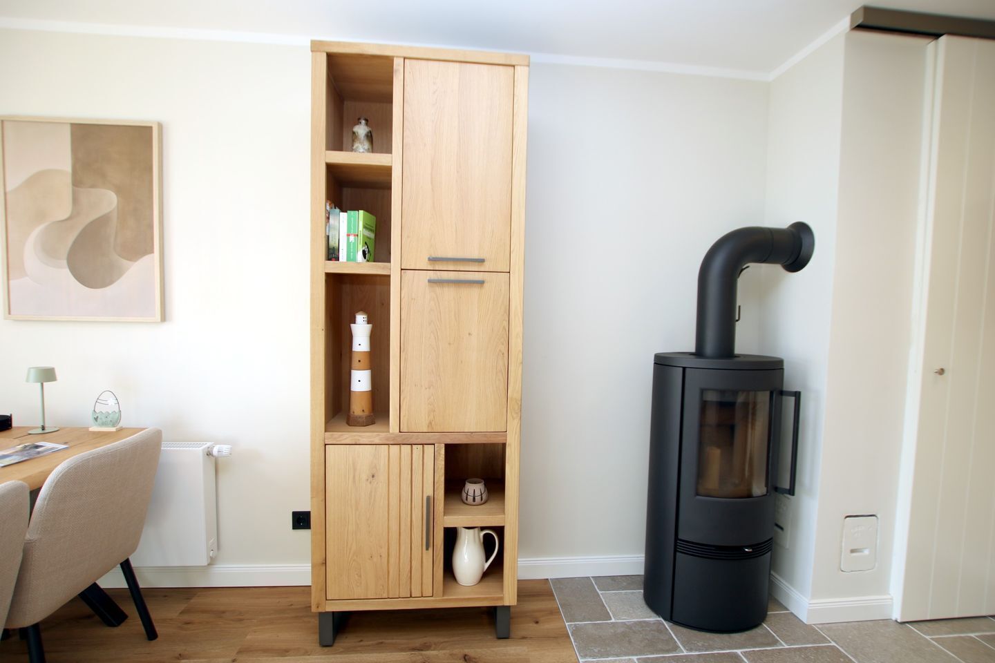Ein Zimmer mit einem Holzkasten, einem schwarzen Herd, einem Tisch mit Stühlen und einem Heizkörper.