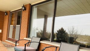 A patio with two chairs and a table, a sliding glass door, and a brick wall. - Beautiful upper unit countryside large cozy rooms near Niagara Falls (Welland)