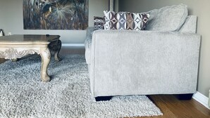 A living room with a grey sofa, patterned pillows, a wooden coffee table, and a large abstract painting on the wall. - Beautiful upper unit countryside large cozy rooms near Niagara Falls (Welland)