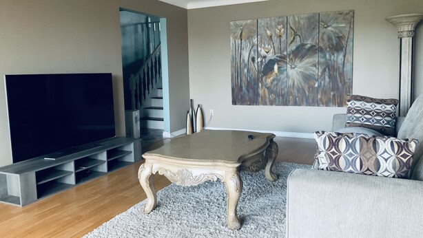 A living room with a flat-screen TV, a coffee table, a sofa, and a staircase. - Beautiful upper unit countryside large cozy rooms near Niagara Falls (Welland)