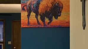 Una habitación con pared azul, un cuadro de un bisonte y una cruz de madera.