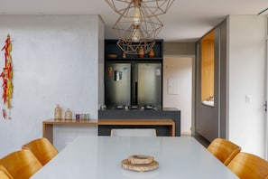 A modern kitchen with a built-in refrigerator, a wooden dining table, and a hanging light fixture.