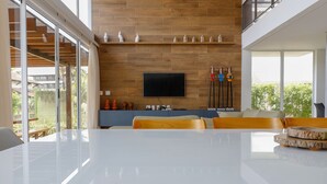 A modern living room with a large white table, wooden flooring, a mounted TV, and a balcony with a view. - WONDERFUL HOUSE - HIGH WALL/ PORTO DE GALINHAS (IPojuca)