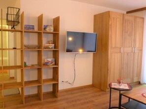 Ein Zimmer mit einem Holzbücherregal, einem an der Wand befestigten Fernseher und einem Tisch mit Unterlage.