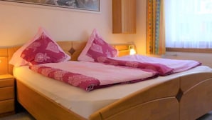 A hotel room with a bed, a nightstand, a lamp, a painting on the wall, and a window with curtains. - Mont-Blanc by Interhome (Zermatt)