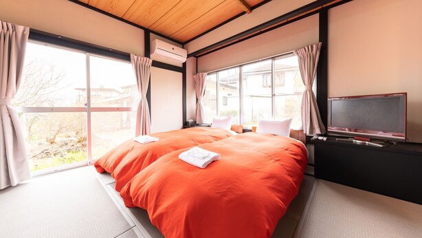 A hotel room with a large bed, a TV, and a window with curtains. - Izu Workation (Ito)