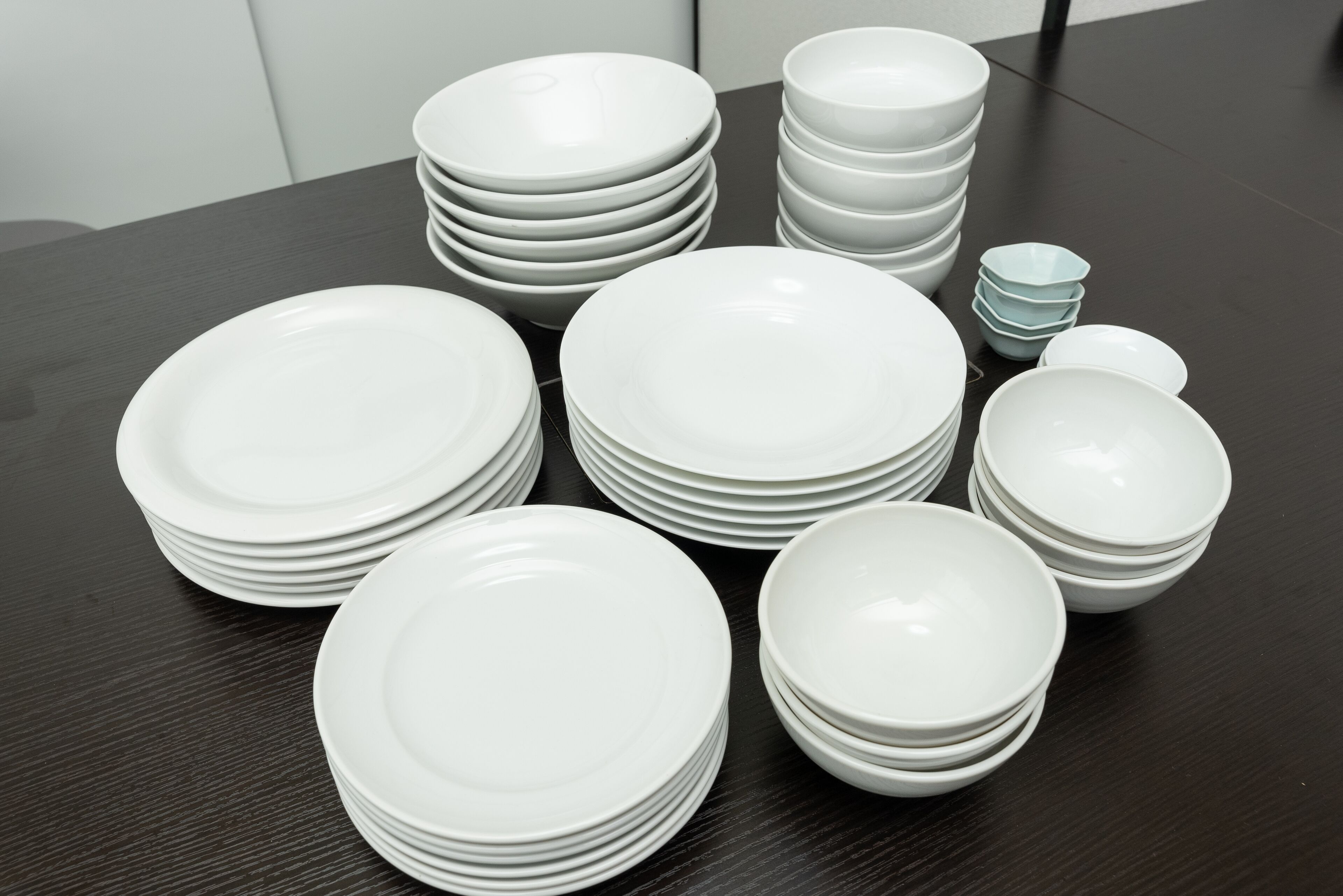 Una mesa con varias pilas de platos y tazones blancos.