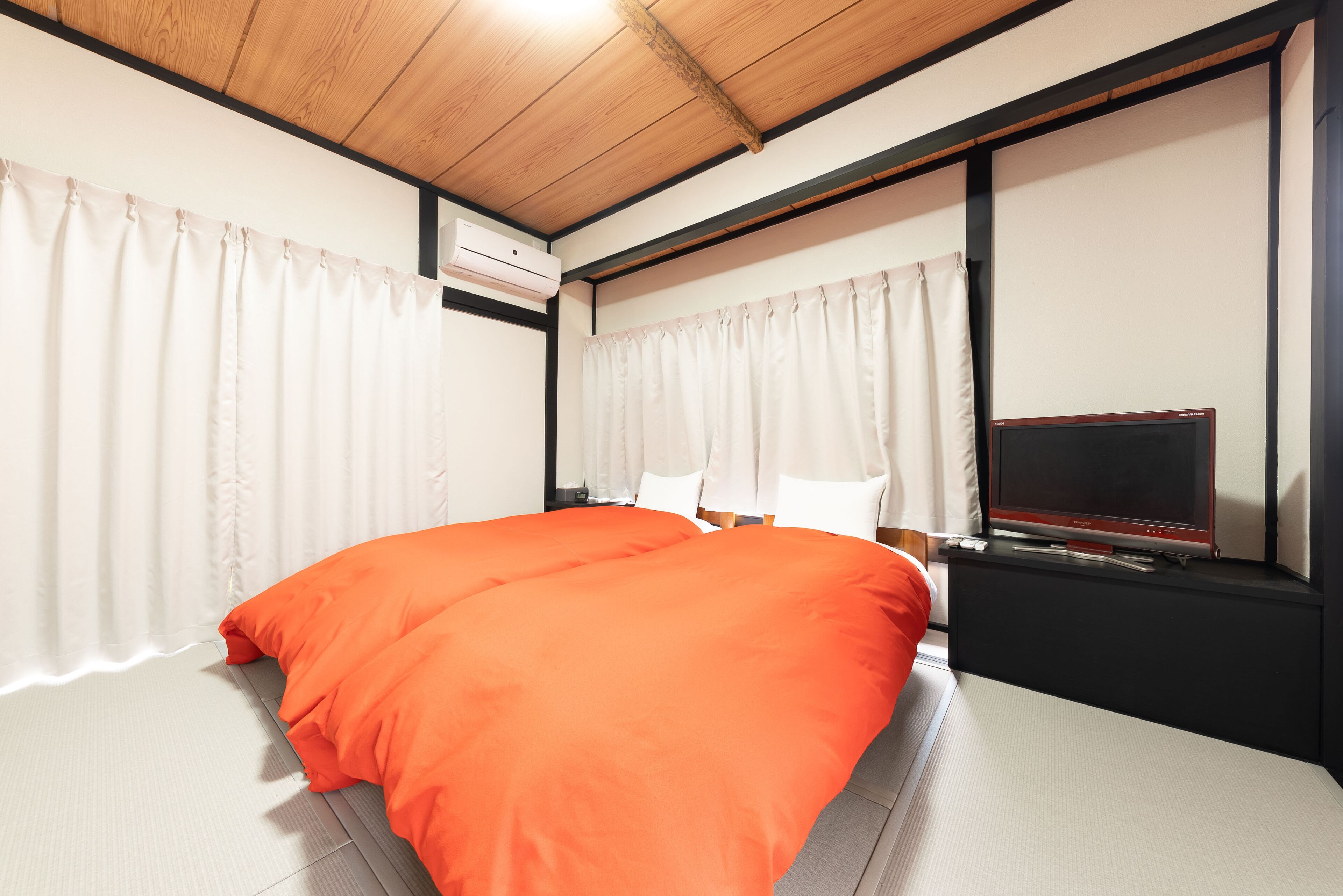 A hotel room with a bed, a TV, and an air conditioning unit.