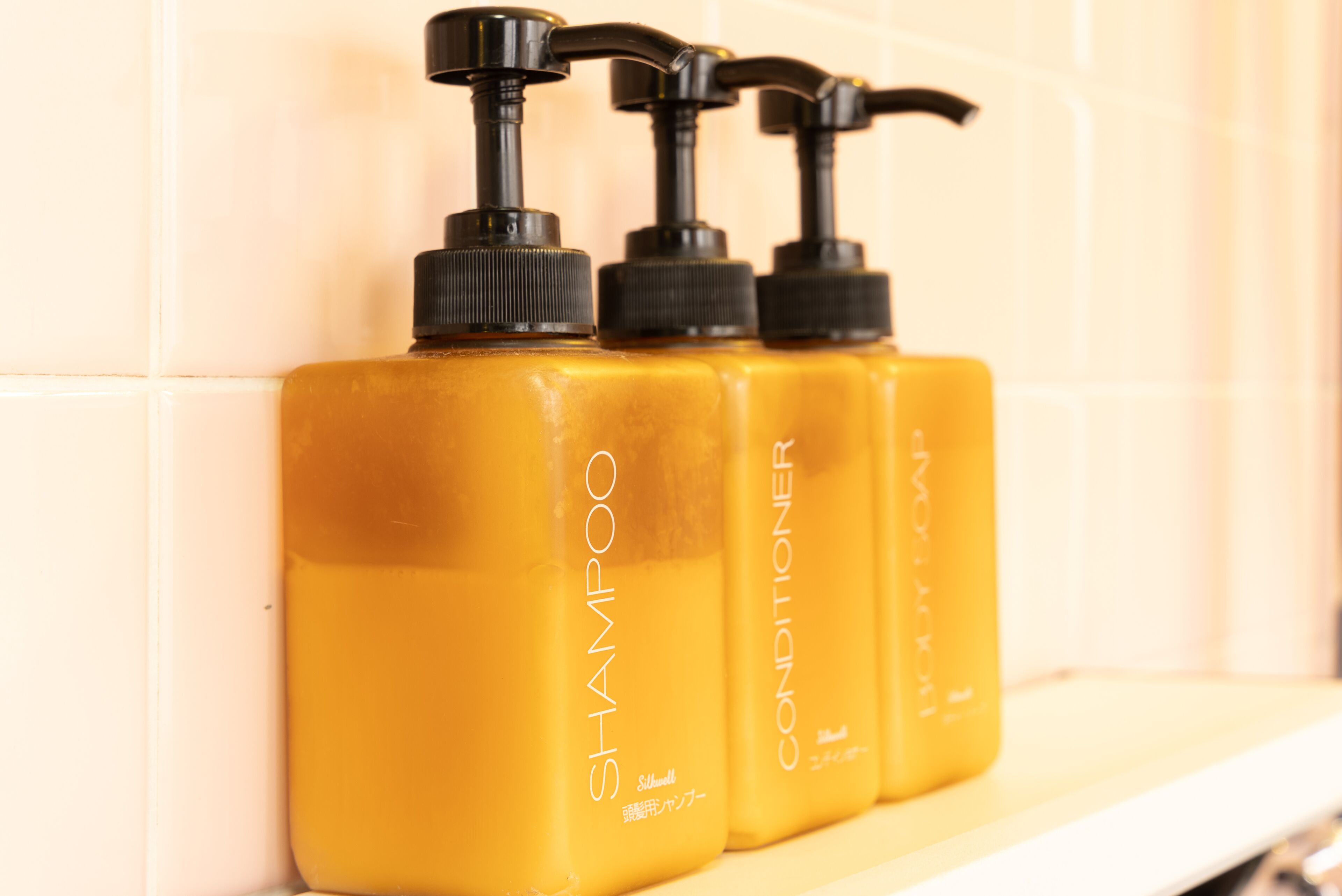 Three bottles of shampoo and conditioner on a shelf.