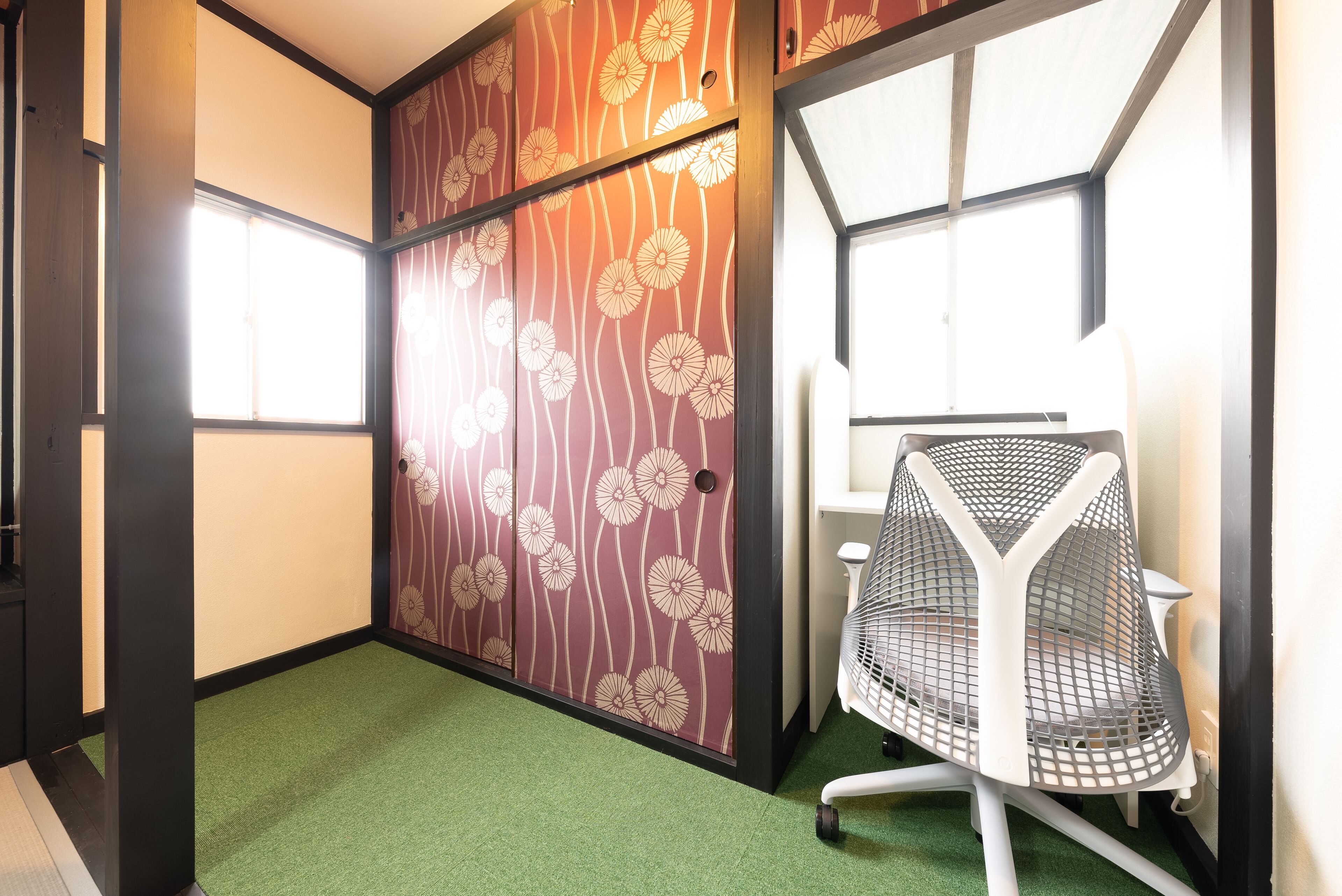 A room with a green carpet, a white chair, and a sliding door with a floral pattern.