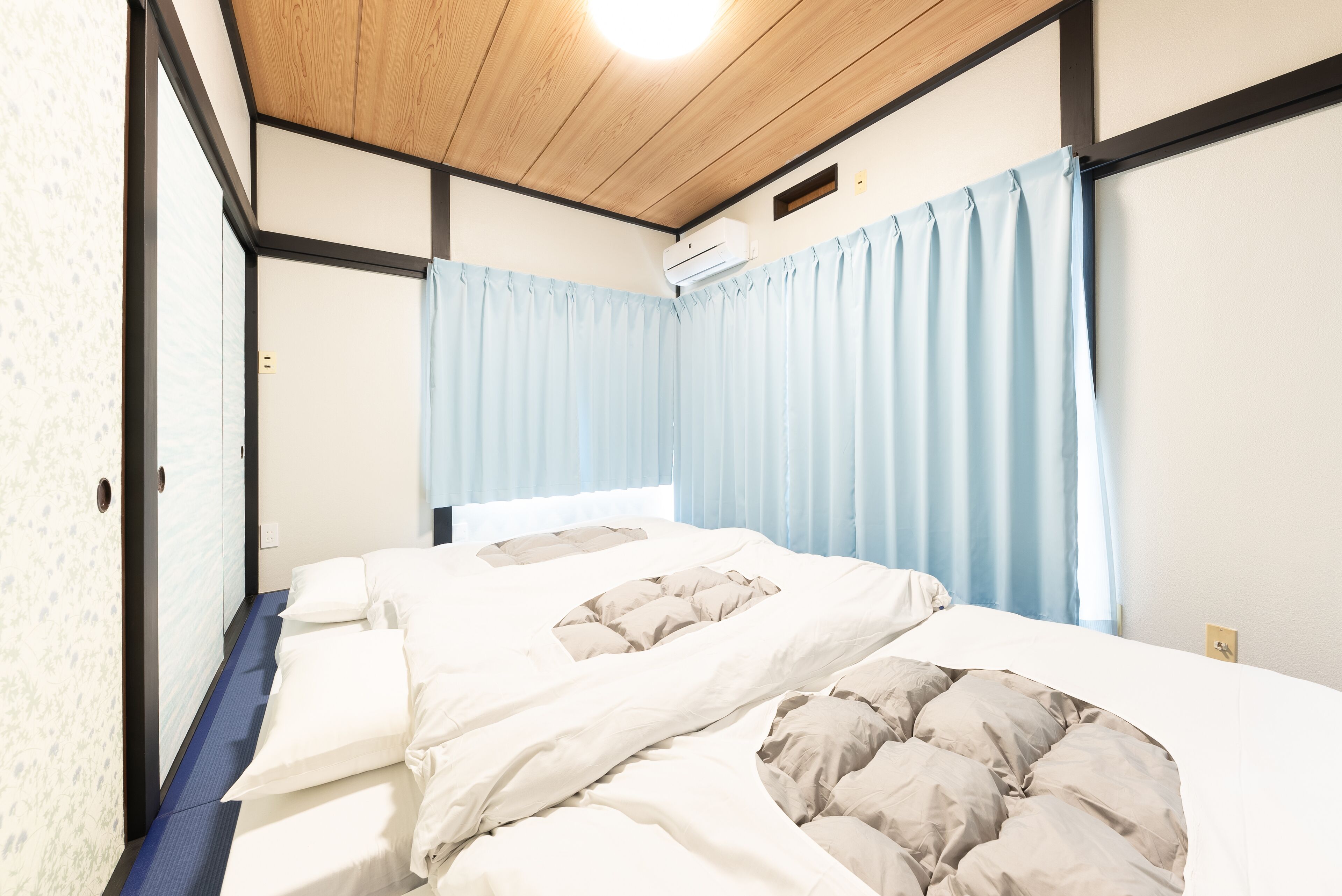 Un dormitorio con cama, ventana con cortinas, lámpara de techo y unidad de aire acondicionado.