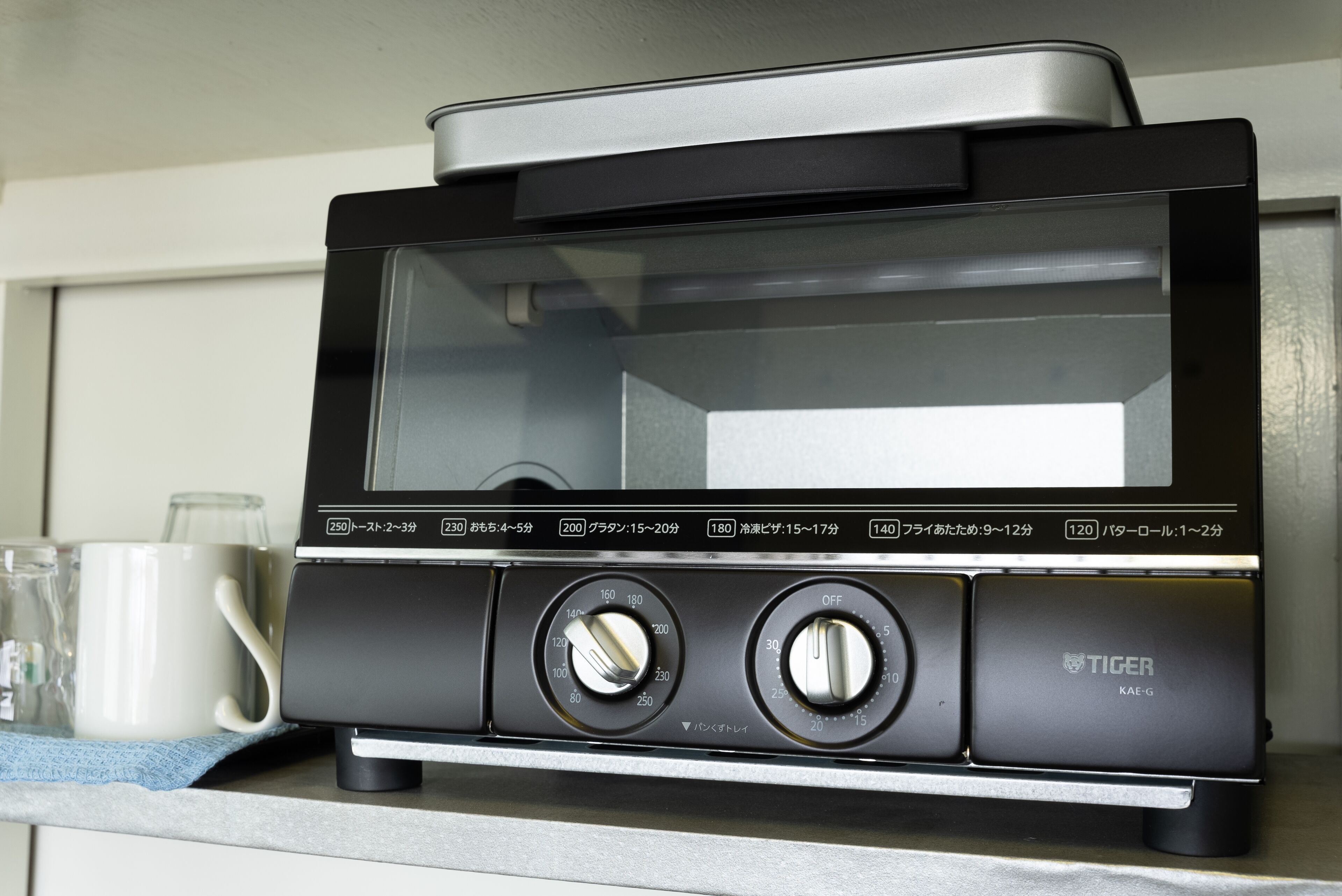 Een keuken met een zwart toaster-oven op het aanrecht, een witte mok en een glazen pot.