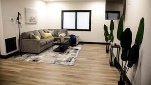 Een moderne woonkamer met een grijze hoekbank, een salontafel en een groot raam.