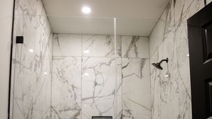 Een moderne douche met een glazen deur, marmeren wanden en een vloer met een rasterpatroon.