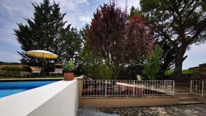 Una piscina con una cerca blanca, un patio de piedra y un árbol de hojas rojas.
