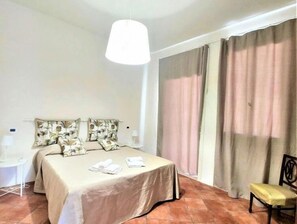 A hotel room with a bed, two pillows, a bedside table, a chair, and a window with curtains.