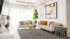 Un soggiorno moderno con un divano bianco, un tavolino in vetro, un tappeto bianco e nero e un grande quadro astratto appeso al muro.