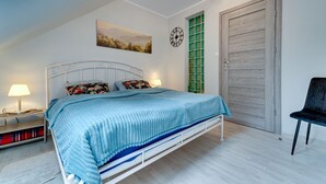 A bedroom with a bed, bedside lamps, a painting, a clock, and a door. - Karpacz Boczna (poddasze) by Interhome (Karpacz)