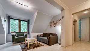 A modern living room with a sofa, armchair, and coffee table. There is a window with curtains and a view of trees. - Karpacz Boczna (poddasze) by Interhome (Karpacz)