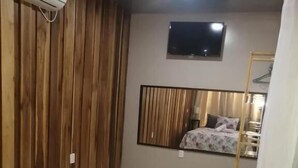 A bedroom with a bed, a wooden wall, a tiled floor, a mirror, and a TV on the wall. - HOTEL VILLAS MYA Puerto Viejo Limon CR (Cahuita)