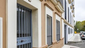 Un edificio residenziale con facciata beige, ampie finestre con inferriate e un vialetto lastricato.