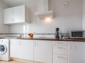 A modern kitchen with white cabinets, a washing machine, a coffee maker, and a microwave.