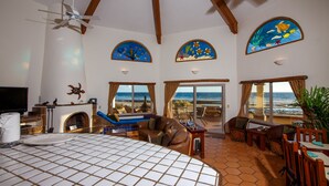 Quarto espaçoso com uma cama grande, um ventilador de teto e vista para o oceano pelas janelas.