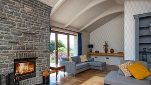 A cozy living room with a stone fireplace, a grey sofa, and a wooden coffee table. - Kingsley Lake View & Paddocks - A group retreat with hot tubs, sports bars & spectacular lake views (Chew Stoke)