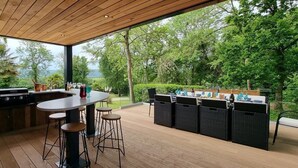 An outdoor kitchen with a dining area, bar stools, and a view of the surrounding greenery. - Kingsley Lake View & Paddocks - A group retreat with hot tubs, sports bars & spectacular lake views (Chew Stoke)