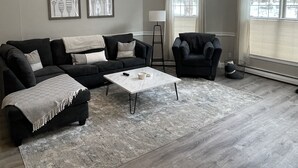 Een ruime woonkamer met een modulaire bank, een salontafel en een groot raam dat voor veel daglicht zorgt.