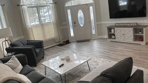 Een ruime woonkamer met een grote bank, een salontafel en een flatscreen tv aan de muur.