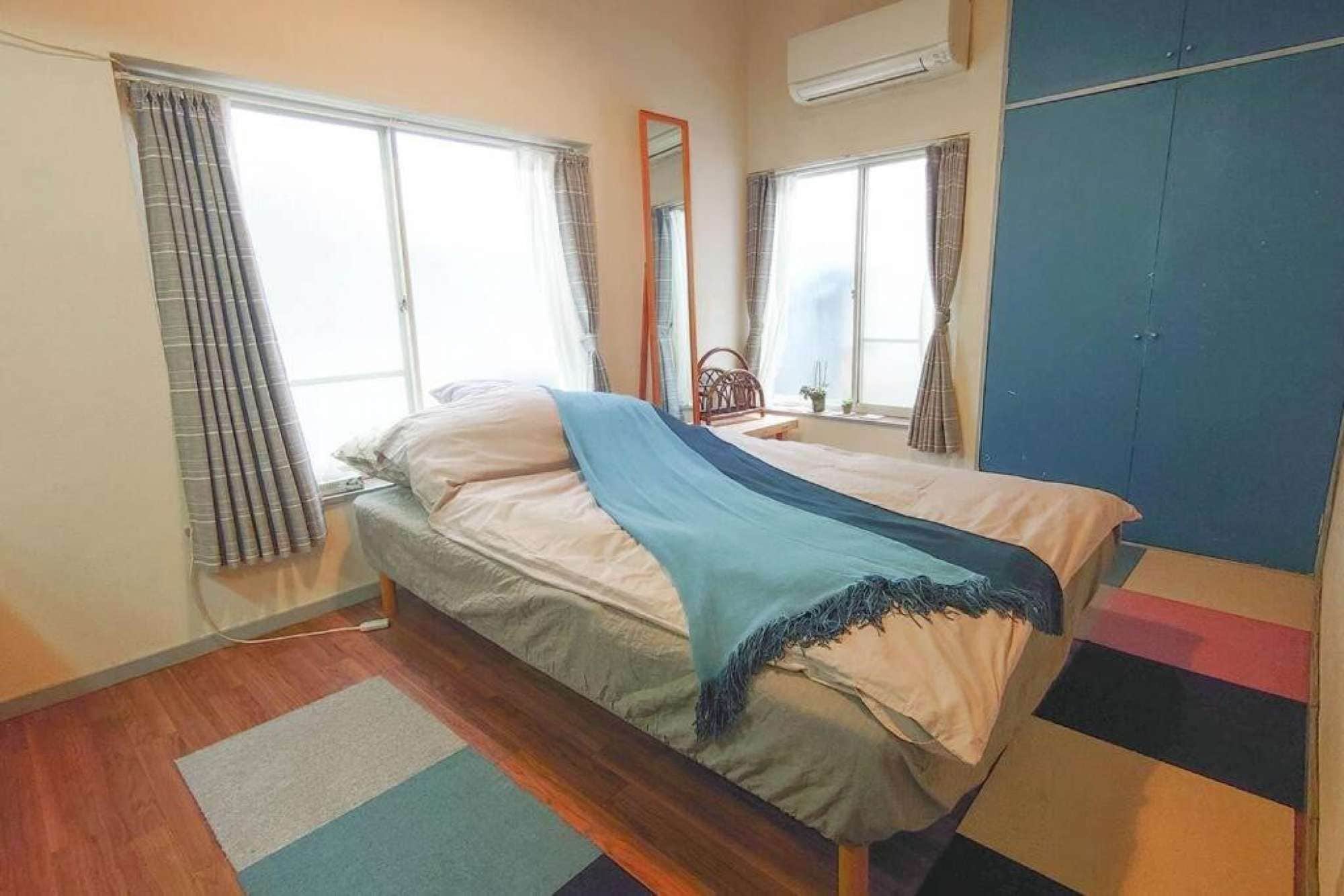 Un lit simple avec une couverture bleue, un plancher en bois et une fenêtre avec des rideaux.