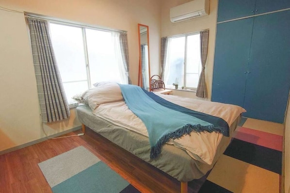 Una cama individual con un edredón azul, suelo de madera y una ventana con cortinas.