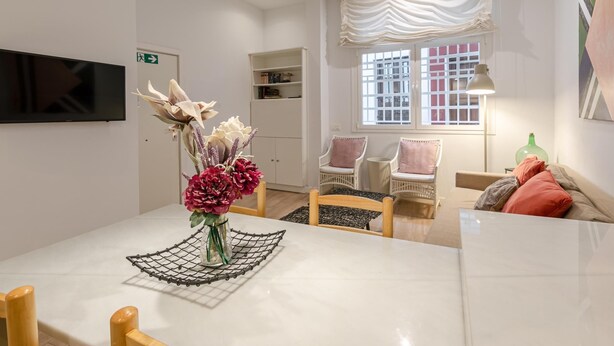 A modern room with a marble table, wicker chairs, a TV, a window with curtains, and a green lamp. - Plaza del Pan Deluxe 1 (Sevilla)