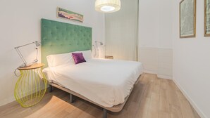 A bedroom with a bed, a green headboard, a bedside lamp, a floor lamp, and a painting on the wall. - Plaza del Pan Deluxe 1 (Sevilla)