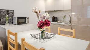 A modern kitchen with a white countertop, a coffee machine, and a decorative flower arrangement on the table. - Plaza del Pan Deluxe 1 (Sevilla)