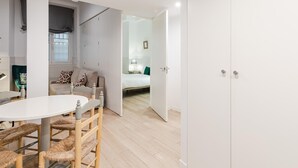 A modern, minimalist room with a round dining table, wicker chairs, a sofa with patterned cushions, and a bed with a green pillow. - Plaza del Pan Deluxe 2 (Sevilla)
