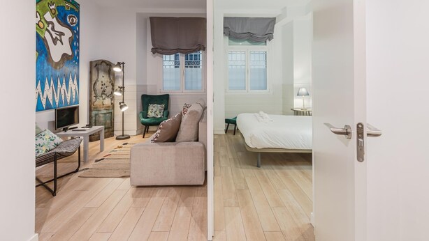 A modern bedroom with a bed, a chair, a desk, and a painting. - Plaza del Pan Deluxe 2 (Sevilla)