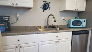 Eine Küche mit weißen Schränken, einer Edelstahlspüle, einer blauen Mikrowelle und einer Kaffeemaschine.
