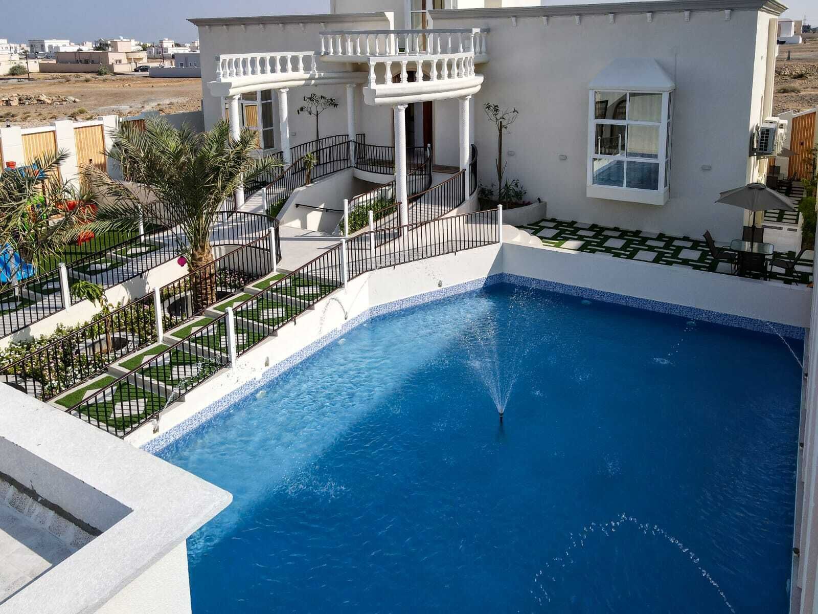 A pool area with a clear blue pool, a white building with balconies, and a landscaped garden with palm trees.