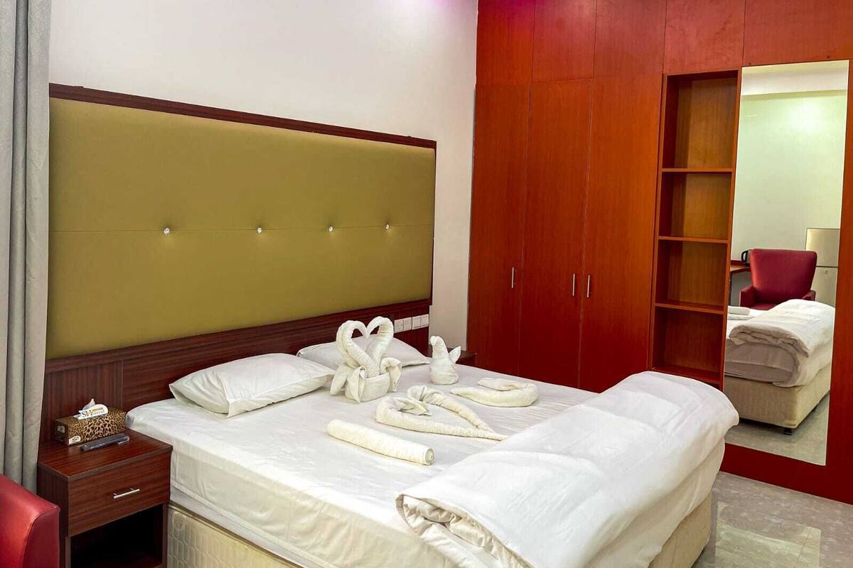 A hotel room with a large bed, a wooden headboard, a wardrobe, and a red armchair.