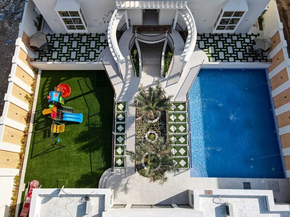 A modern house with a swimming pool, a children's play area, and a well-maintained lawn.