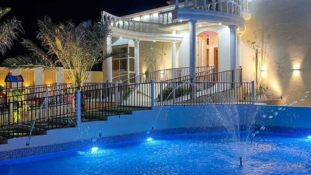 A nighttime view of a hotel with a swimming pool, a covered patio area, and a well-lit entrance. - Discovery Guest House -Sur (Sur)