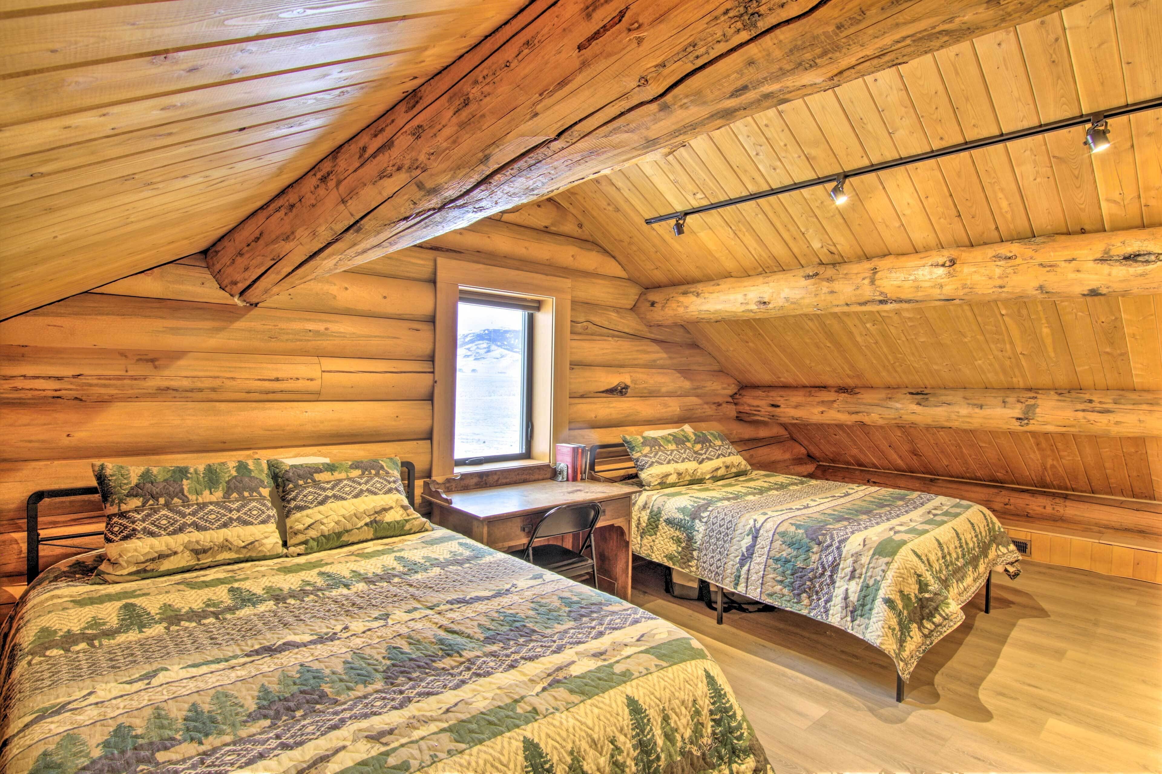 A log cabin bedroom with two beds, a desk, and a window.