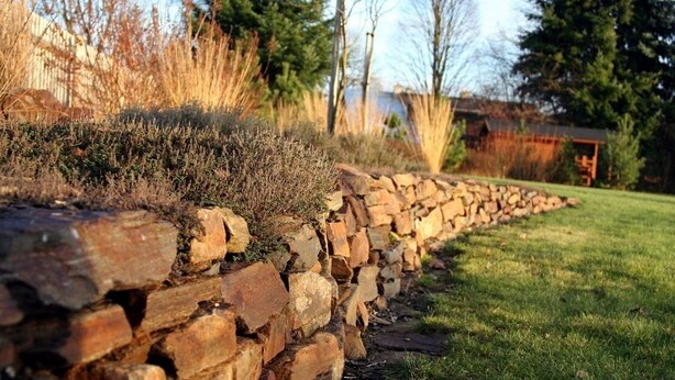 A stone wall with a grassy area and trees in the background. - Newly built cottage with pool and  large fenced garden (Ždár nad Sázavou)