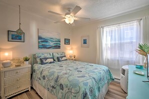 Un dormitorio con cama, ventilador de techo, cómoda, ventana con cortinas y decoración en la pared.