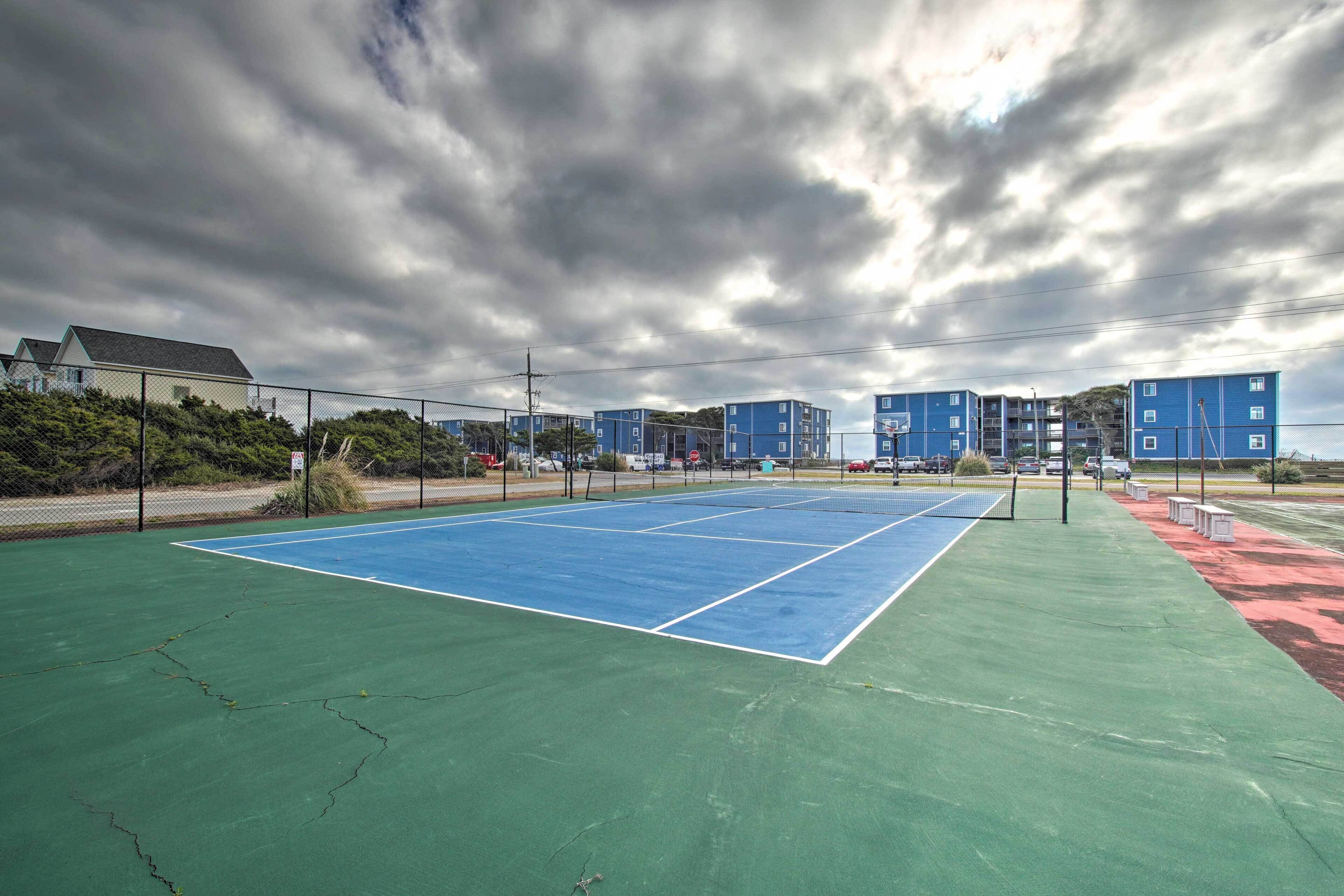 Un court de tennis aux surfaces vertes et bleues, entouré d’une clôture et avec des bâtiments en arrière-plan.