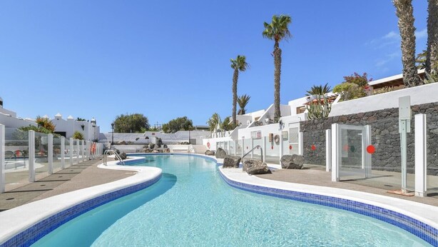 Una piscina con agua cristalina azul, rodeada de edificios blancos y palmeras.